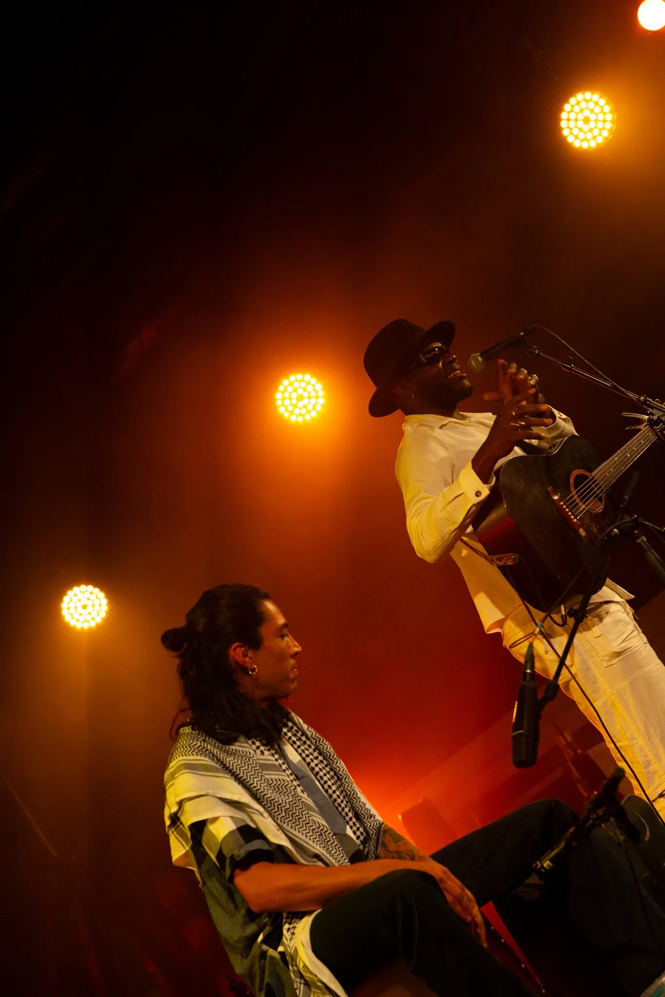 Twee MC's op een openluchtpodium voor een dicht publiek, met de Basiliek van Koekelberg op de achtergrond.