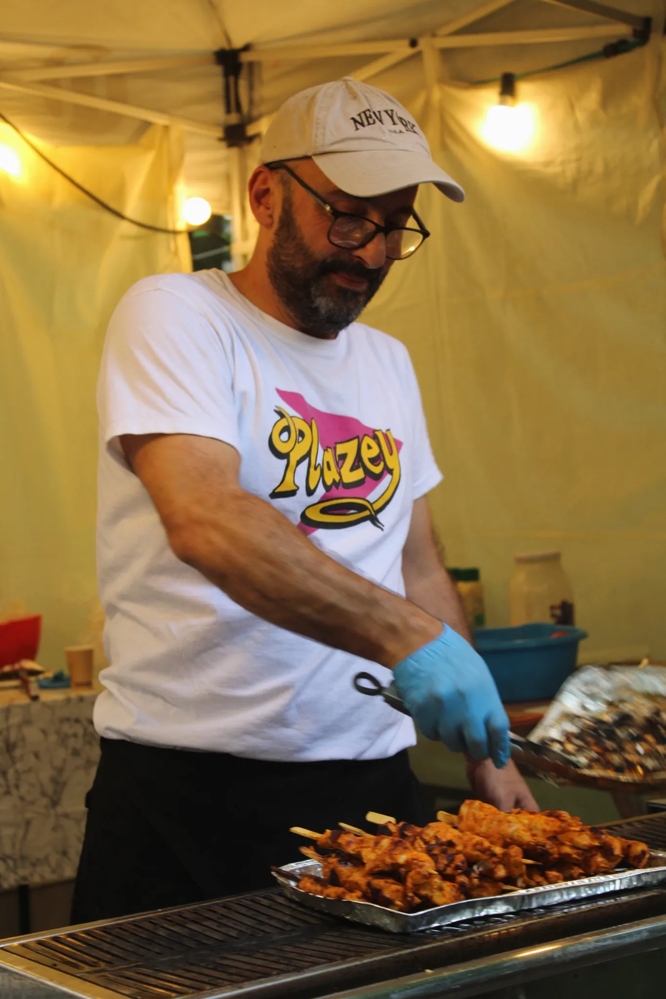 Un·e bénévole en t-shirt Plazey grille des brochettes à un stand extérieur.