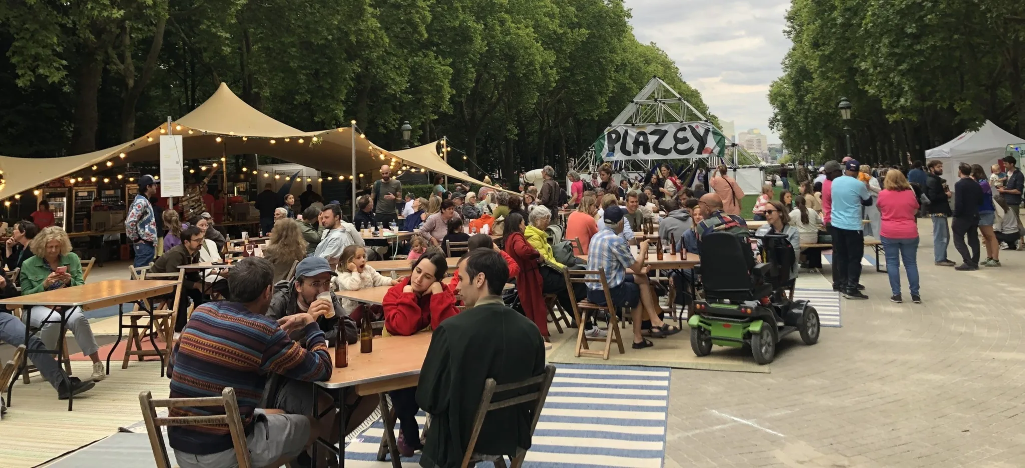 Het Plazey-festivalterrein in het Elisabethpark: picknicktafels, slingers, en het Plazey-bord tussen de bomen.