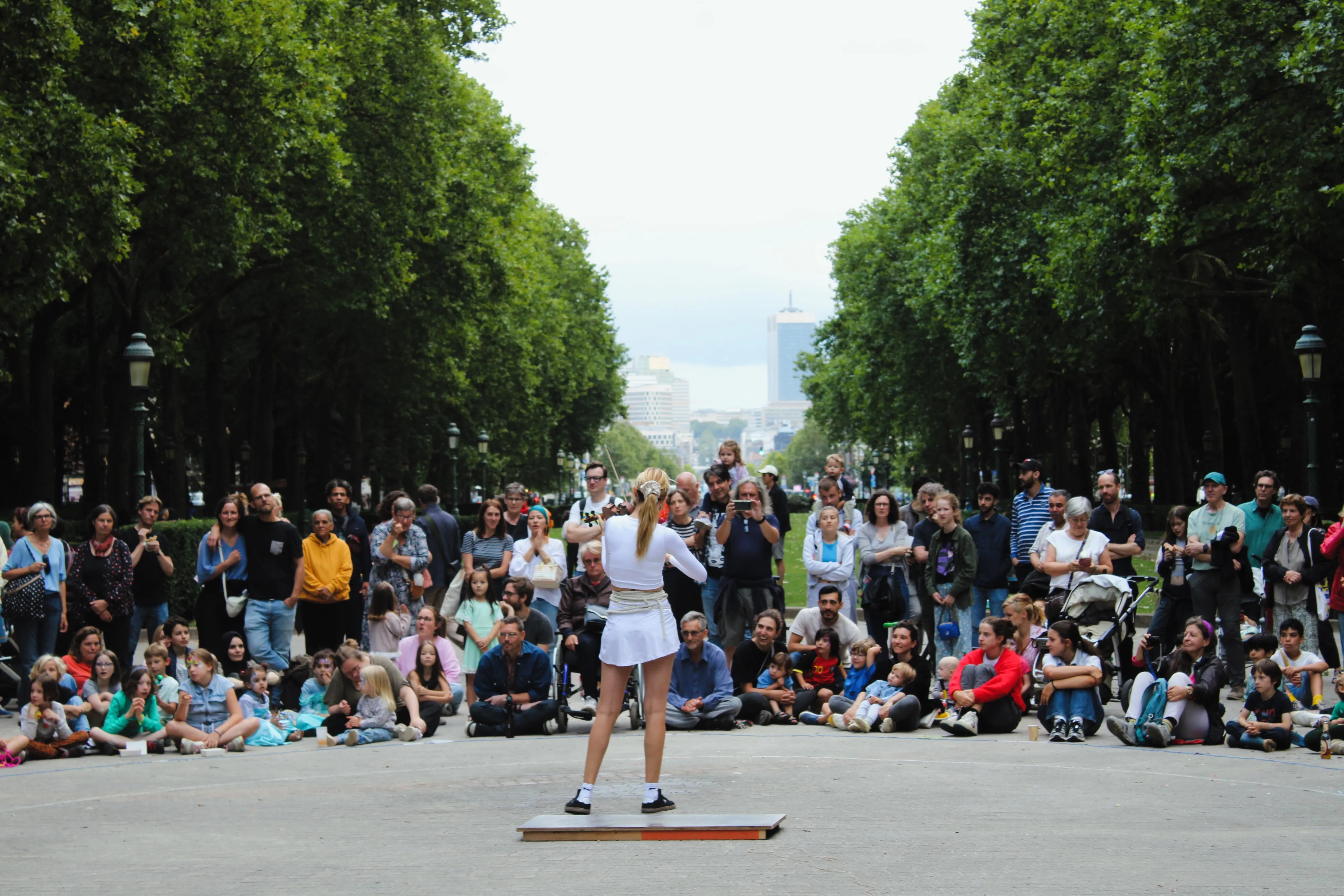 Un public suit un spectacle de rue, avec une personne en fauteuil roulant au premier rang parmi les autres visiteurs.