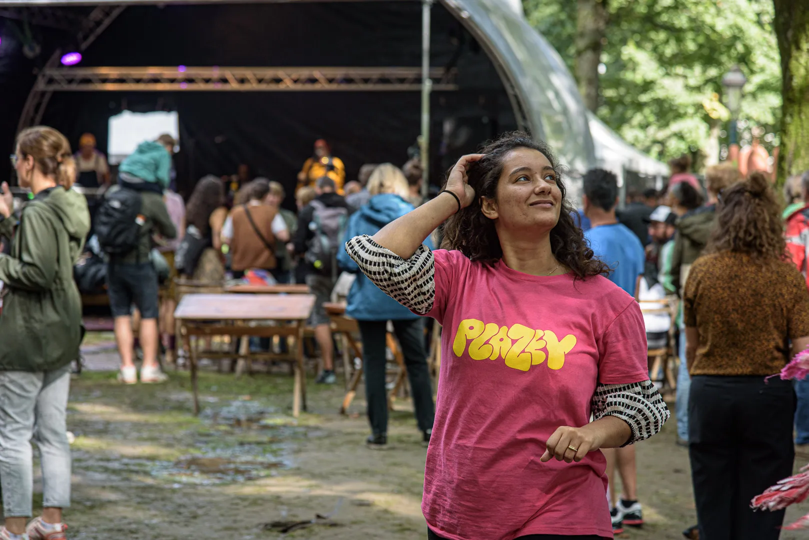 Een vrijwilliger in roze Plazey-t-shirt kijkt omhoog, met het festivalterrein achter haar.