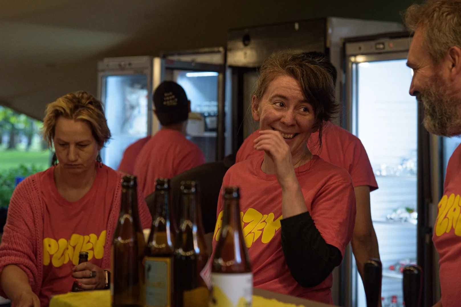 Vrijwilligers in roze Plazey-t-shirt achter de bar.